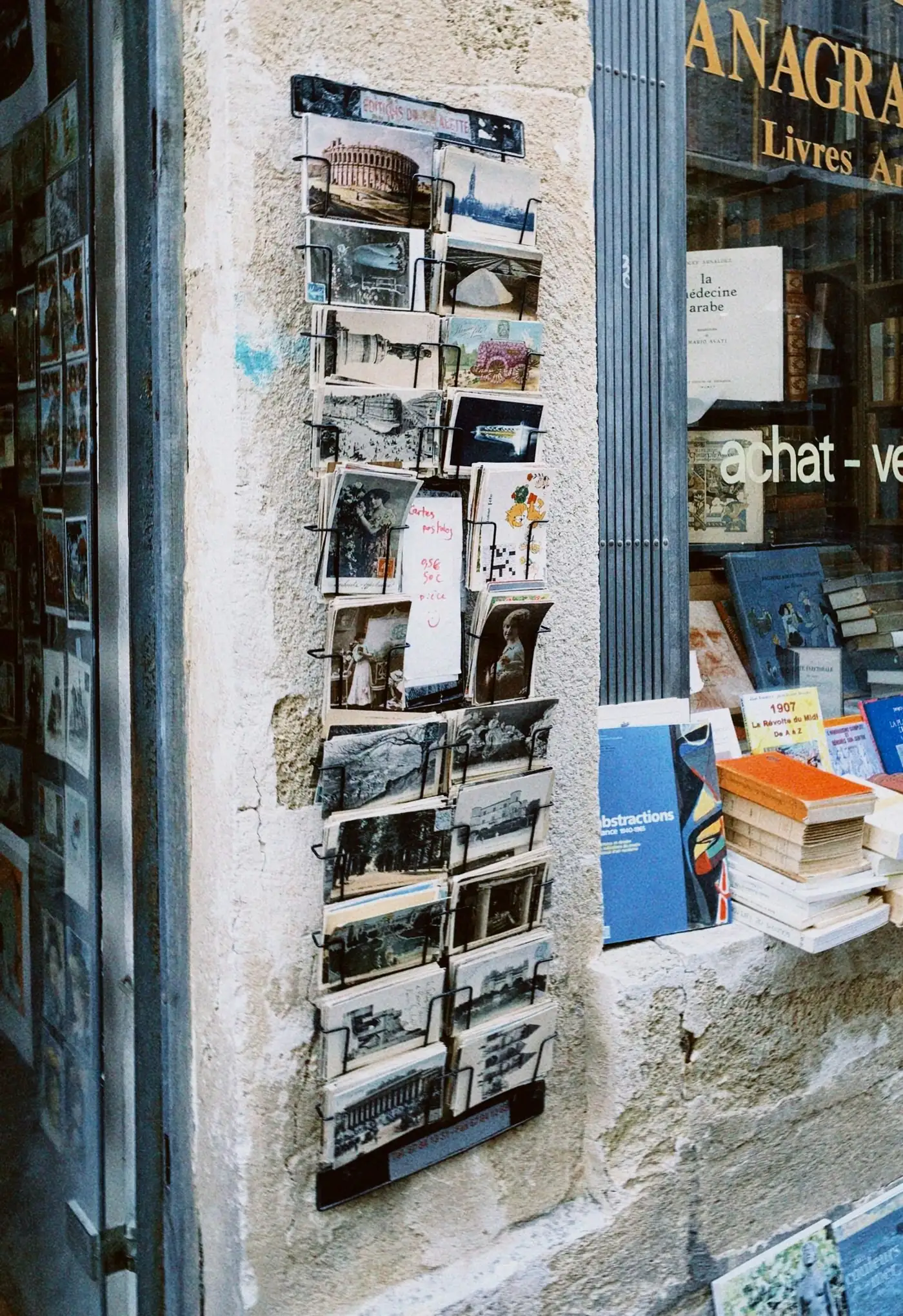 A wire rack of vintage postcards displayed on a stone pillar outside a shop